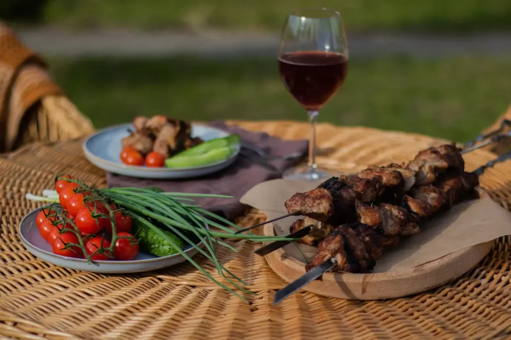 Une table sur laquelle est posée des brochettes, un verre de vin et des assiettes d'accompagnement de légumes