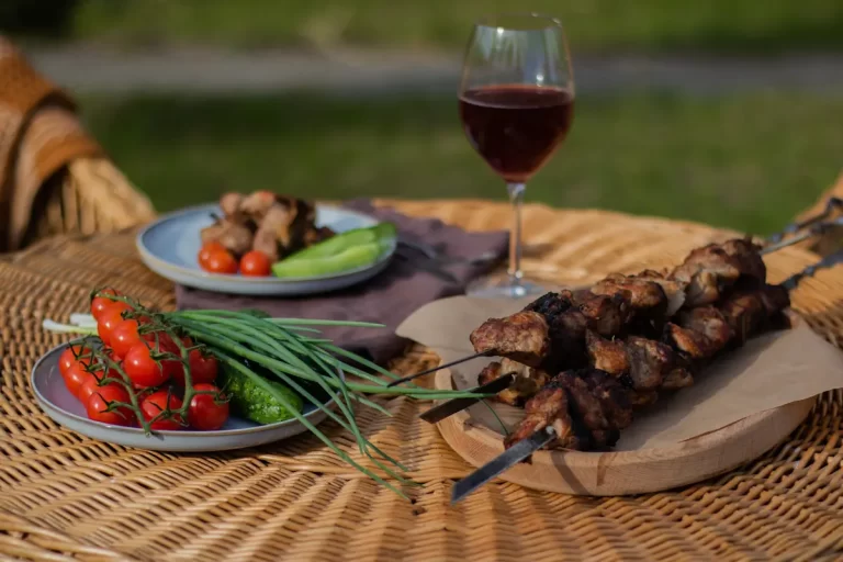 Une table sur laquelle est posée des brochettes, un verre de vin et des assiettes d'accompagnement de légumes