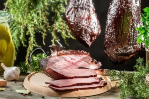 Une assiette qui présente des tranches de jambons secs devant des jambons sec qui tiennent en l'air