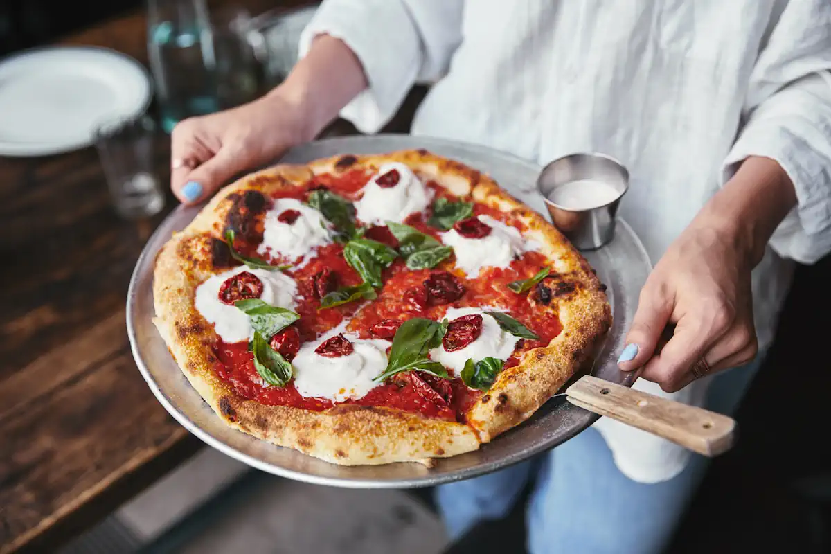 Une personne qui sert une pizza napolitaine sur une assiette avec une sauce