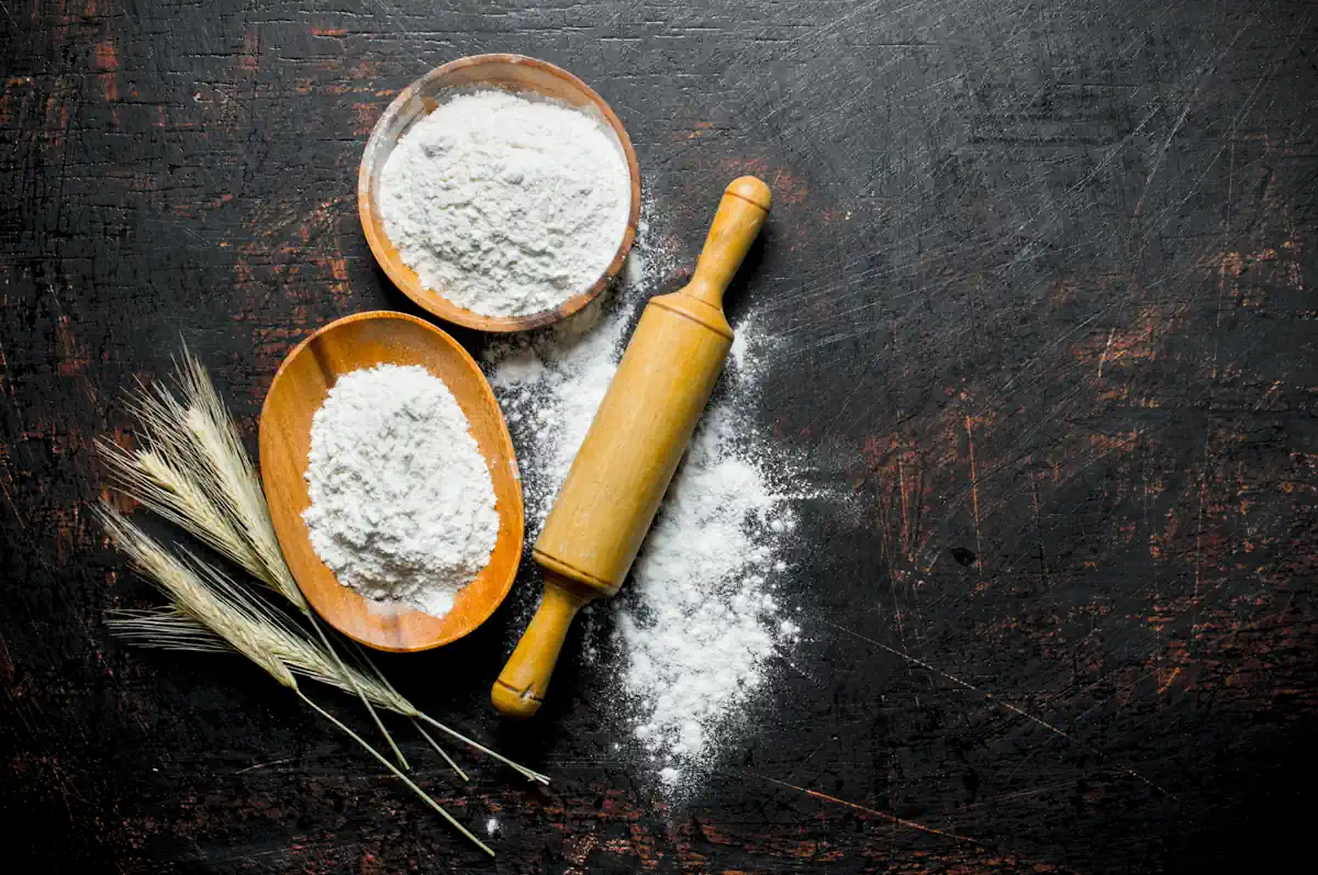 Deux bols contenant des farines à côté de grains de blés et d'un rouleau