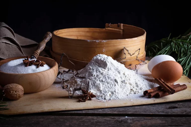 De la farine à côté d'un œuf et d'un tamis et d'un vol de sucre
