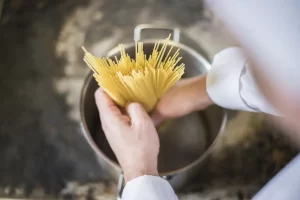 Un chef en tenue qui verse des pâtes dans un casserole