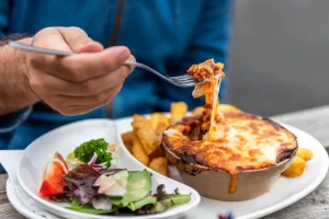 Une personne qui mange une tartiflette posée près d'une salade