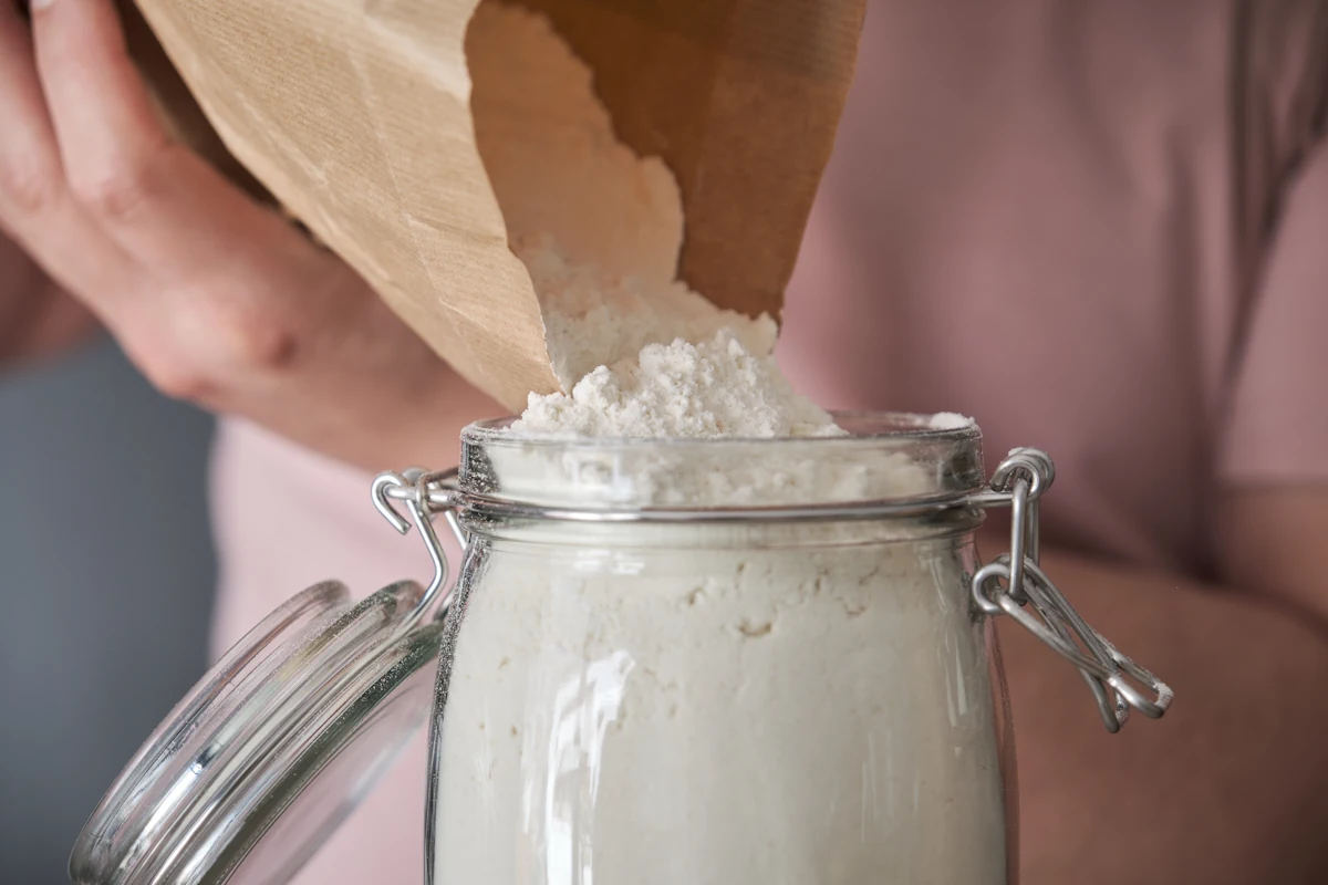 Une personne qui verse de la farine dans un bocal en verre