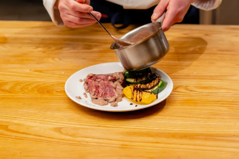 Une personne qui prépare une assiette de filet de veau avec des légumes et de la sauce