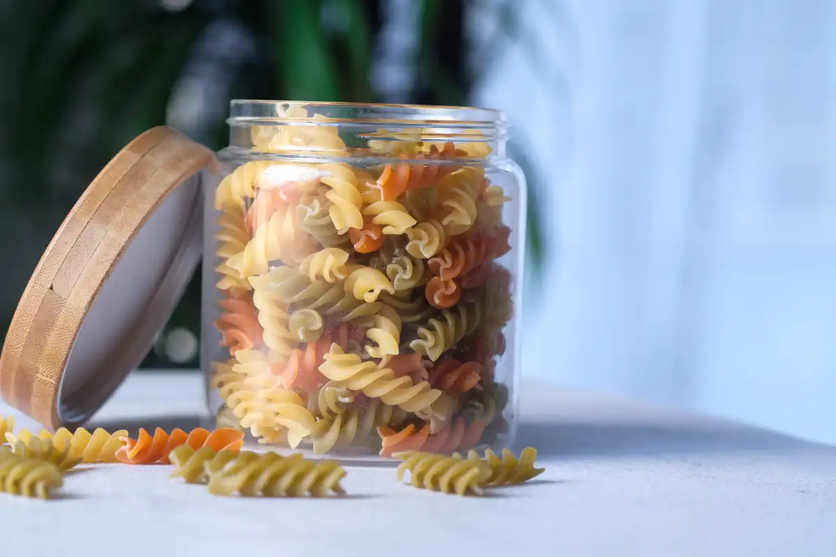 Des pâtes de différente couleurs dans un bocal en verre posé sur la table