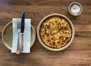 Une tartiflette dans un bol posé à côté de couverts